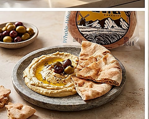 Rahma pita torn beside a plate of hummus with olive oil and olives.
